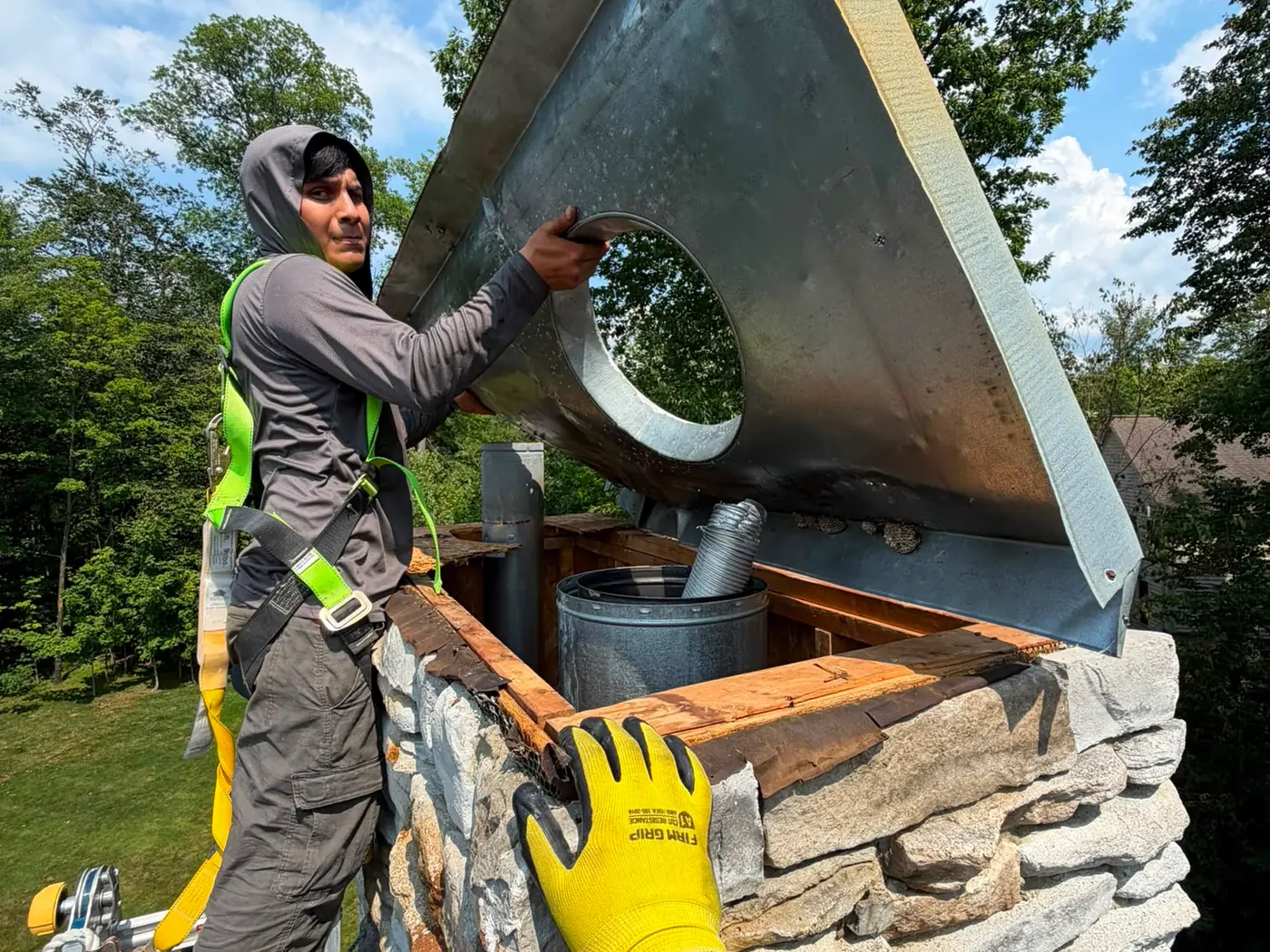 Chimney technician in uniform lifting a metal chase cover into place on a stone chimney