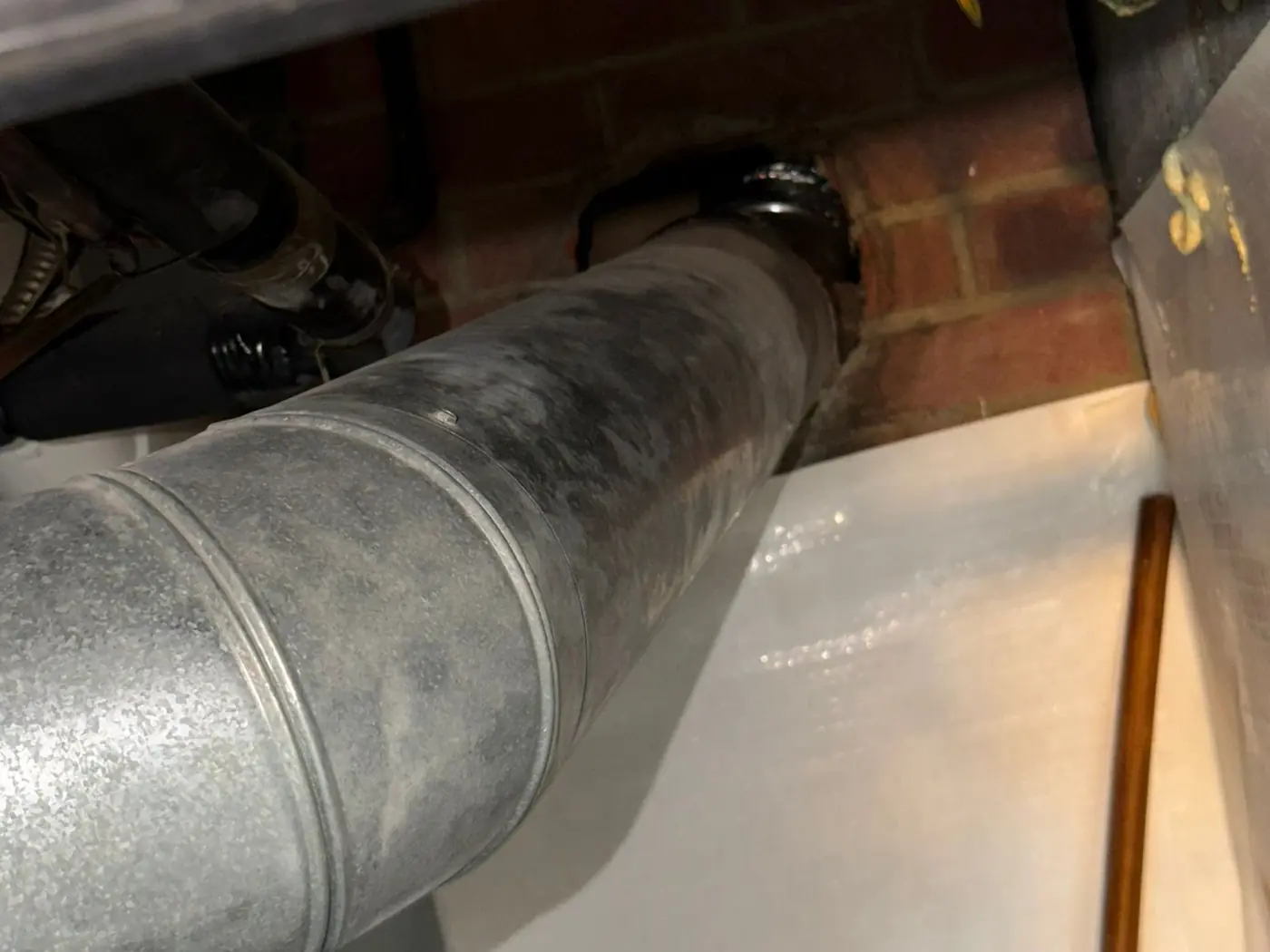 Galvanised vent pipe running from an appliance into a brick chimney wall