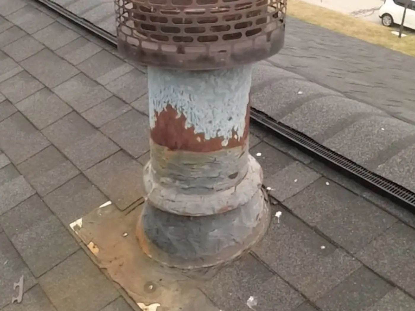 Badly weathered round chimney crown with spalling and exposed aggregate on a shingle roof