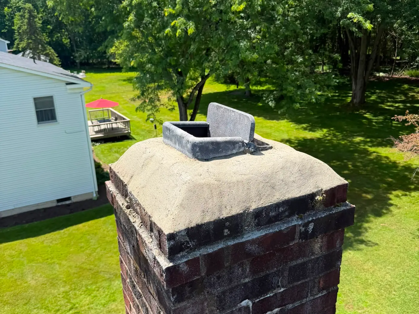 Newly finished chimney crown on a red brick chimney above a shingle roof