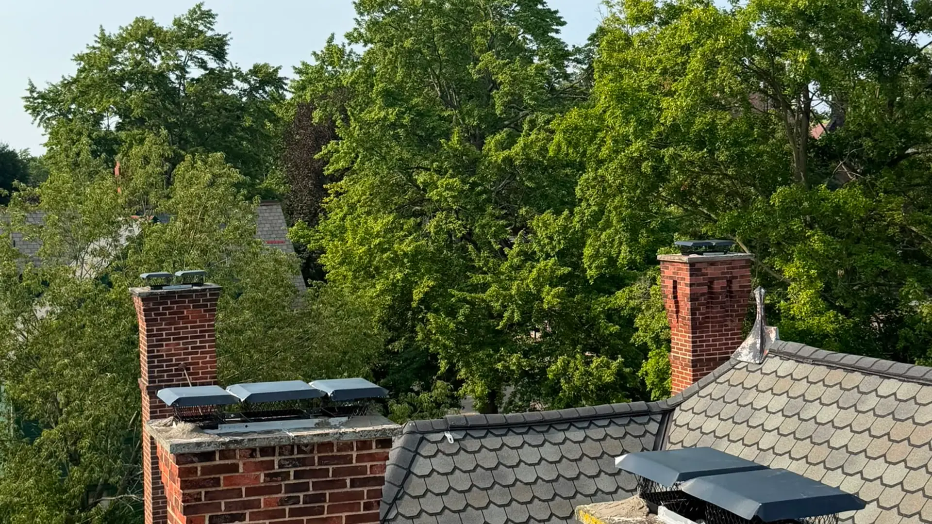 Two capped brick chimneys on the steep slate roofline of a period home